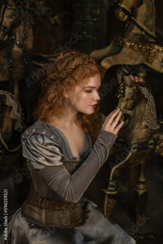 Portrait of a red-haired girl in a gray medieval dress strokes a wooden horse