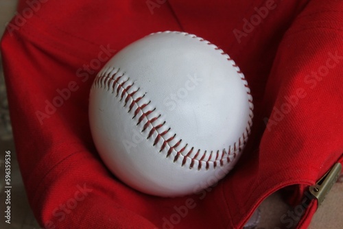 A new baseball lies on a red baseball cap.