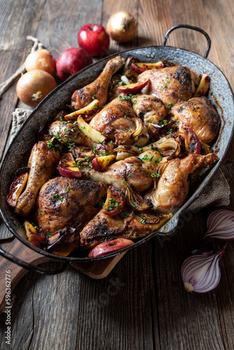 Braised chicken with onions and apples in a old fashioned roasting pan isolated on wooden table