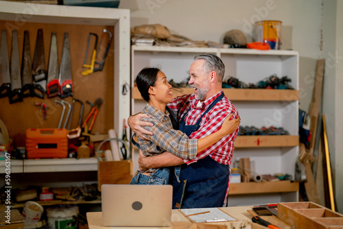 Carpenter lovers stand and hug closely together to celebrate the successful of work in workplace in concept of happiness wood worker family support homemade craft business. photo