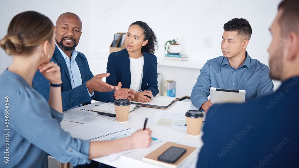 Diverse group of business people talking in a meeting and using technology and paperwork in a boardroom. Team of professionals sitting together, brainstorming and planning a strategy in the office