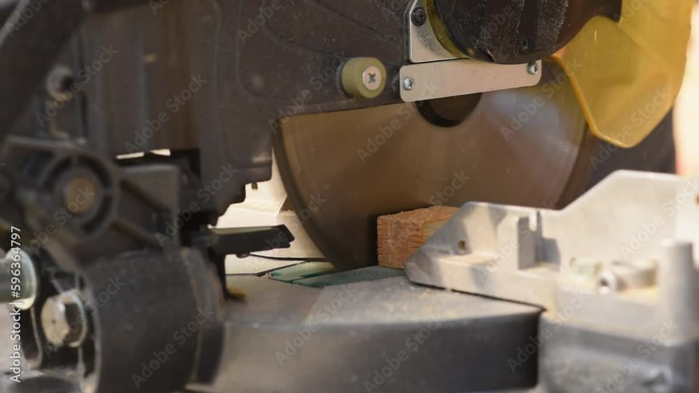 A man uses an electric circular saw to cut wooden bars. Carpenter works on a board outdoors, close-up A man uses an electric circular saw to cut wooden bars. Carpenter works on a board outdoors, close-up