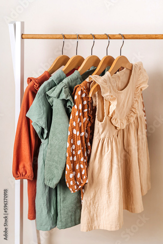 Wallpaper Mural Wooden Clothing Rack with children's outfits close up. Fashion dresses in vintage colors on hangers in wardrobe. Kids wardrobe. Set of kids clothes and accessories for girl. Torontodigital.ca