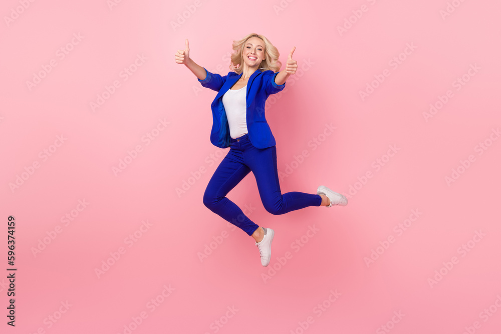 Full length photo of excited shiny lady wear blue jacket showing two thumbs up jumping high isolated pink color background