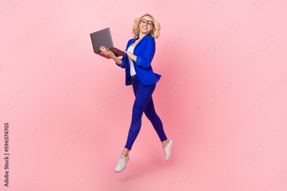 Full length photo of shiny pretty lady wear blue jacket texting modern device jumping high isolated pink color background Full length photo of shiny pretty lady wear blue jacket texting modern device jumping high isolated pink color background