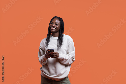 Happy African American woman using smartphone and smiling in studio