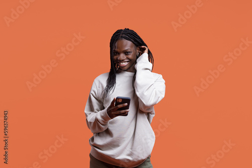 Cheerful black woman with smartphone touching hair in studio