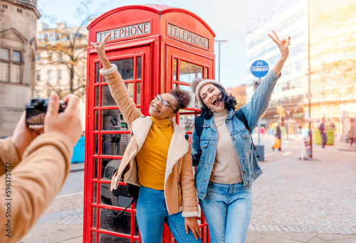 two friend, girlfriend and women using a mobile phone, camera and taking selfie against a red phonebox in the city of England.Travel Lifestyle concept
