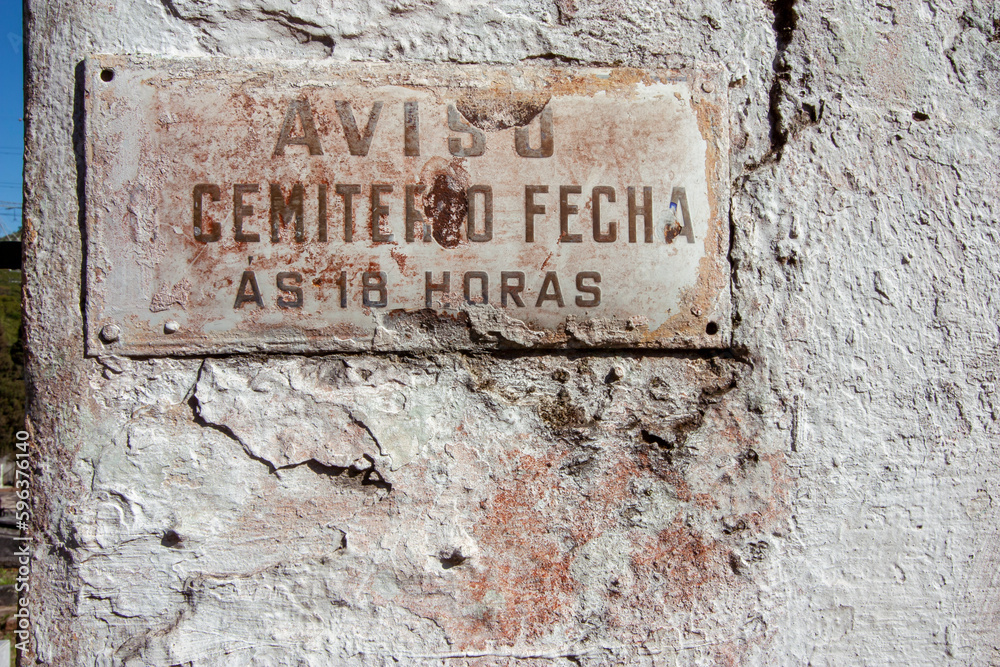 Placa antiga e enferrujada em parede de cemitério com o horário de funcionamento Placa antiga e enferrujada em parede de cemitério com o horário de funcionamento