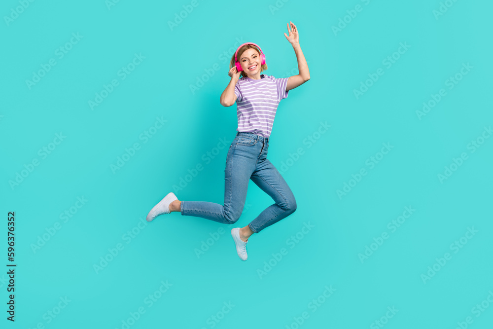 Full length photo of pleasant girl stylish t-shirt denim pants waving hand touching headphones isolated on turquoise color background Full length photo of pleasant girl stylish t-shirt denim pants waving hand touching headphones isolated on turquoise color background
