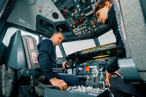 An experienced pilot instructs a young student before a training flight in the cockpit of an aero simulator