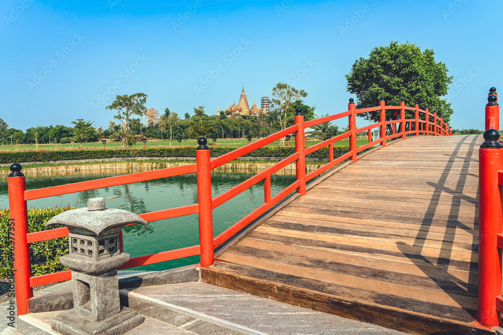 Beautiful view of Japanese style red wooden bridge over emerald pond with fountains against nature of paddy field outdoors. Japanese style garden with unique red wooden bridge. Beautiful landscape. Beautiful view of Japanese style red wooden bridge over emerald pond with fountains against nature of paddy field outdoors. Japanese style garden with unique red wooden bridge. Beautiful landscape.
