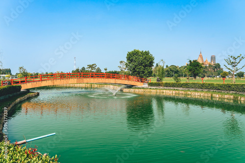 Beautiful view of Japanese style red wooden bridge over emerald pond with fountains against nature of paddy field outdoors. Japanese style garden with unique red wooden bridge. Beautiful landscape.