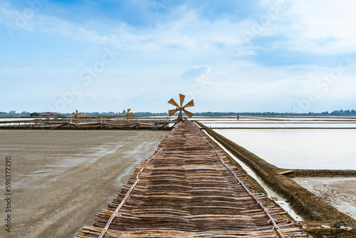 Wooden turbine at salt pan using for press seawater up to field with blue sky background in summer time of Thailand,South East Asia. Beautiful landscape of salt fields.Traditional salt farming culture
