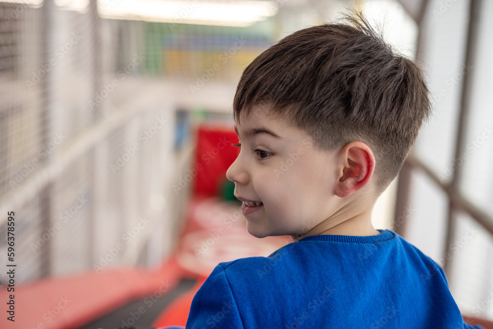 cute adorable child boy playing at playing center playground inside shopping mall.preschooler on top of slide using wheels ring inflatable circle to slide down from artificial hill.hapy smiling kid