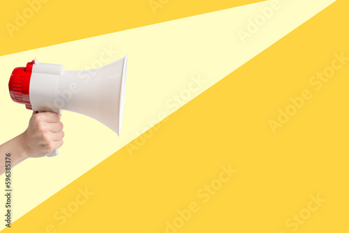 Megaphone in woman hands on a yellolw background.