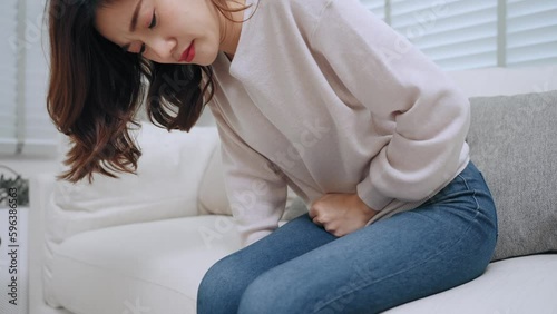 Young Asian woman having menstrual pain on sofa in living room at home