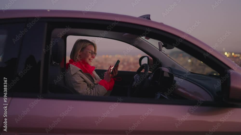Female millennial get good news on mobile phone while sits in car interior. Young woman beaming with joy,  celebrating goal achievement after receiving an approved application with email confirmation