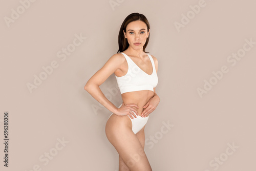 Confident millennial woman posing in underwear on beige background