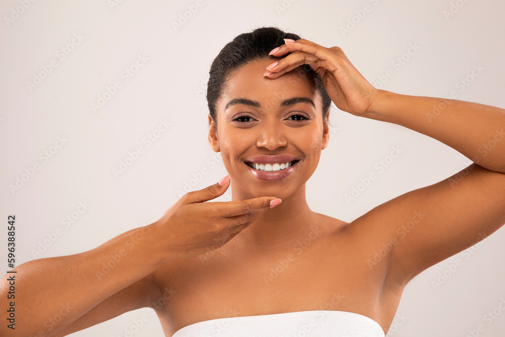 Naklejka premium Cheerful millennial pretty black woman touching her beautiful face