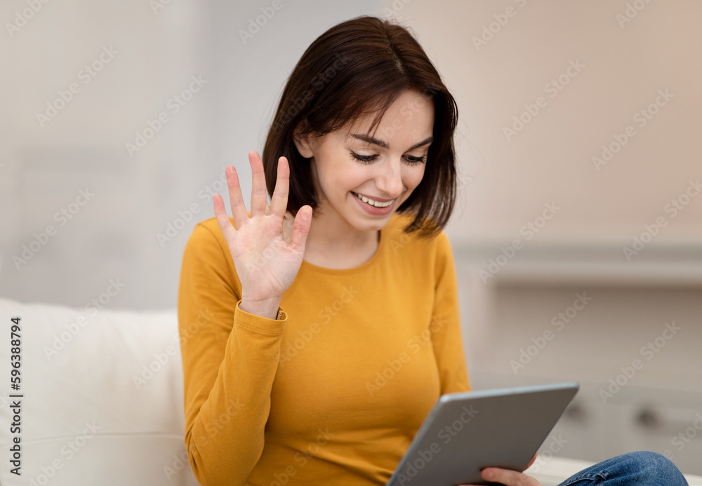 Closeup of cheerful young woman waving at tablet screen Closeup of cheerful young woman waving at tablet screen