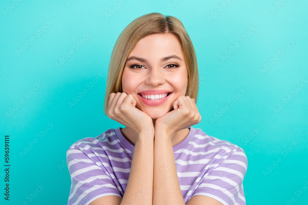 Photo of satisfied positive cute girl short hairstyle striped t-shirt hold fists on cheeks smiling isolated on turquoise color background Photo of satisfied positive cute girl short hairstyle striped t-shirt hold fists on cheeks smiling isolated on turquoise color background