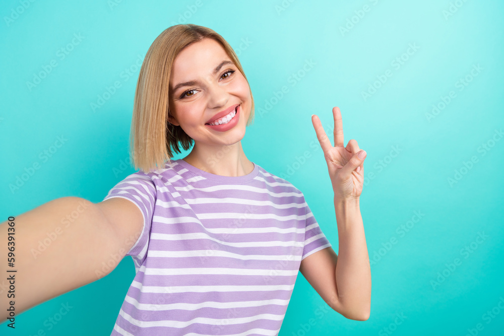 Selfie photo cadre of friendly charming lady wear trendy t-shirt show v-sign toothy beaming smile isolated on aquamarine color background Selfie photo cadre of friendly charming lady wear trendy t-shirt show v-sign toothy beaming smile isolated on aquamarine color background