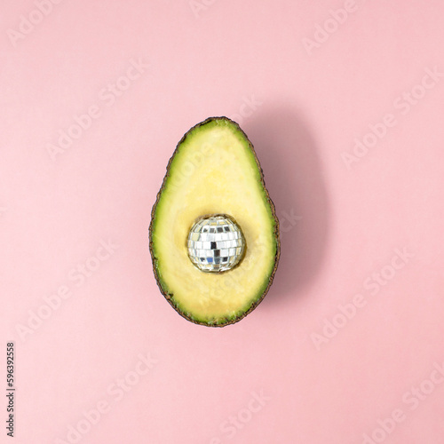 A half of avocado with the disco ball inside on pink background. Modern design. Concept of food
