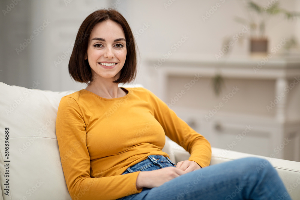 Happy pretty young woman sitting on couch at home Happy pretty young woman sitting on couch at home