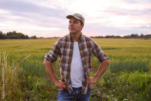 Farmer in front of a sunset agricultural landscape. Man in a countryside field. Country life, food production, farming and country lifestyle concept. © Acronym