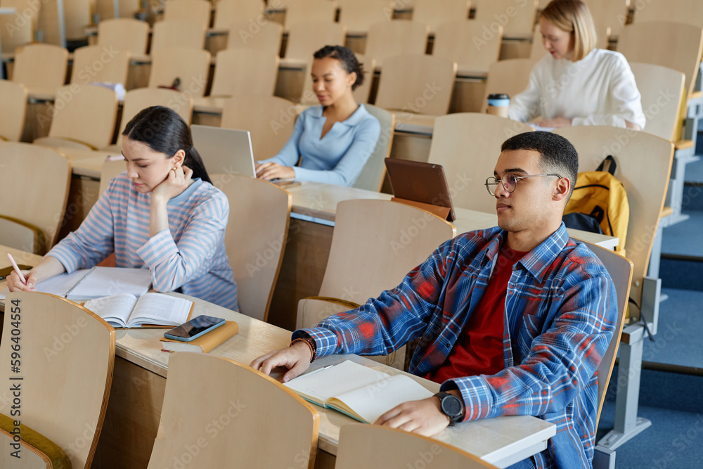 Group of students sitting at desk with books in lecture hall and studying at university