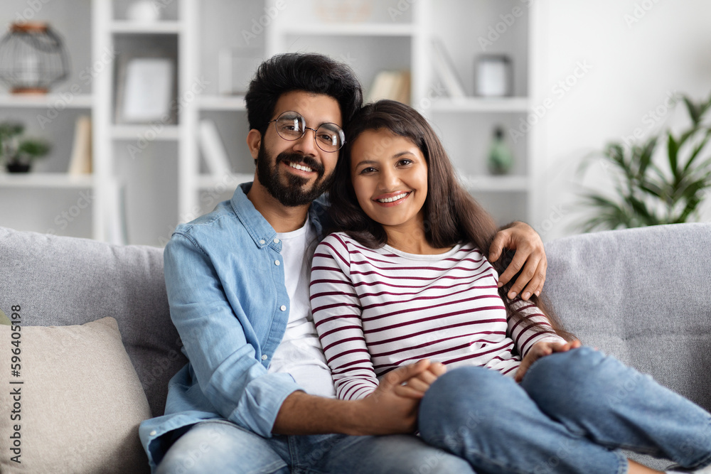 Portrait of cheerful eastern couple cuddling on couch at home