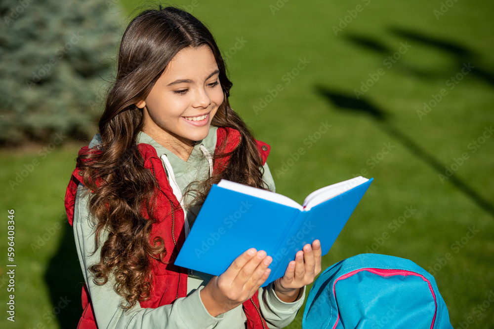 Fototapeta premium photo of positive school teen girl read in park. school teen girl read outdoor.