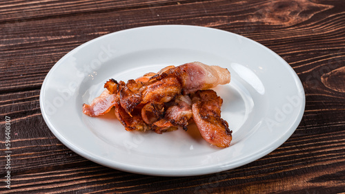Pieces of fried bacon in a plate as an ingredient for breakfast.