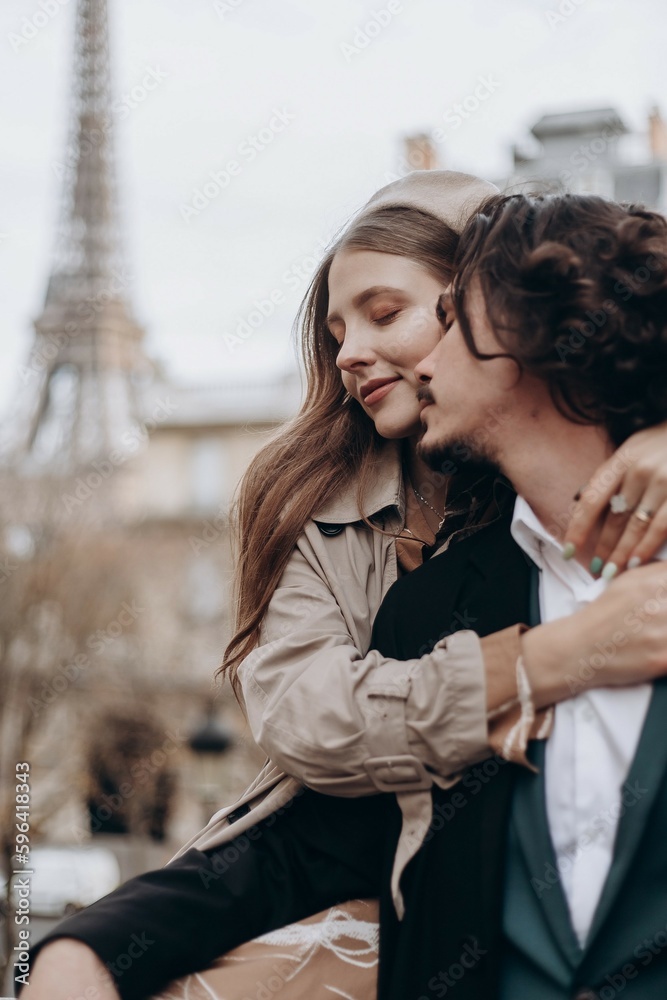 Fototapeta premium A couple in love walks along the streets of Paris, a guy in a coat and a suit, a girl in a dress with a beret and a trench coat in autumn