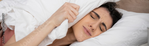 Displeased woman putting pillow on head on bed in morning, banner.