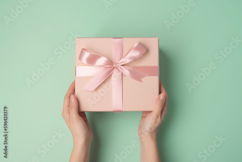 Female hands holding light pink giftbox on the green mint background. Generative AI
