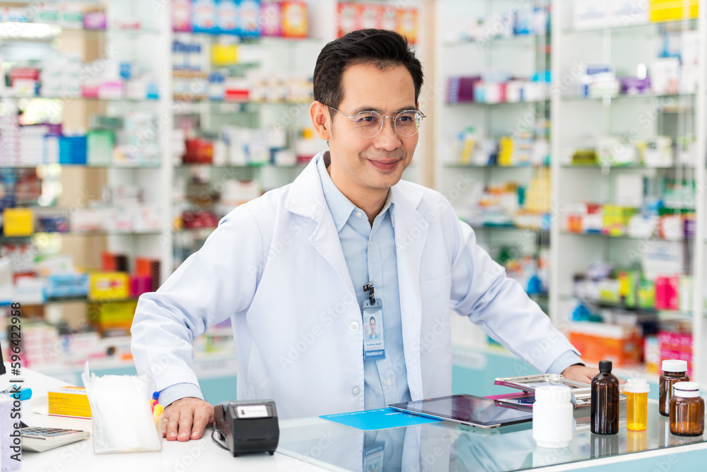Professional pharmacist asian man smiling at counter using digital tablet for check medicine inventory in drug store, Medical service online, Telemedicine to giving medical information to patient.
