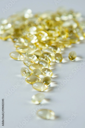 The deposit of transparent capsules with vitamin D or Omega-3 in blurry focus are on a gray background. Vertical image.