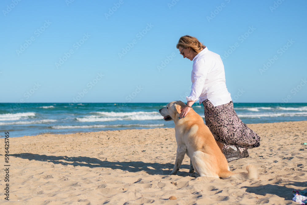Woman petting her Labrador retriever on the beach at sunset