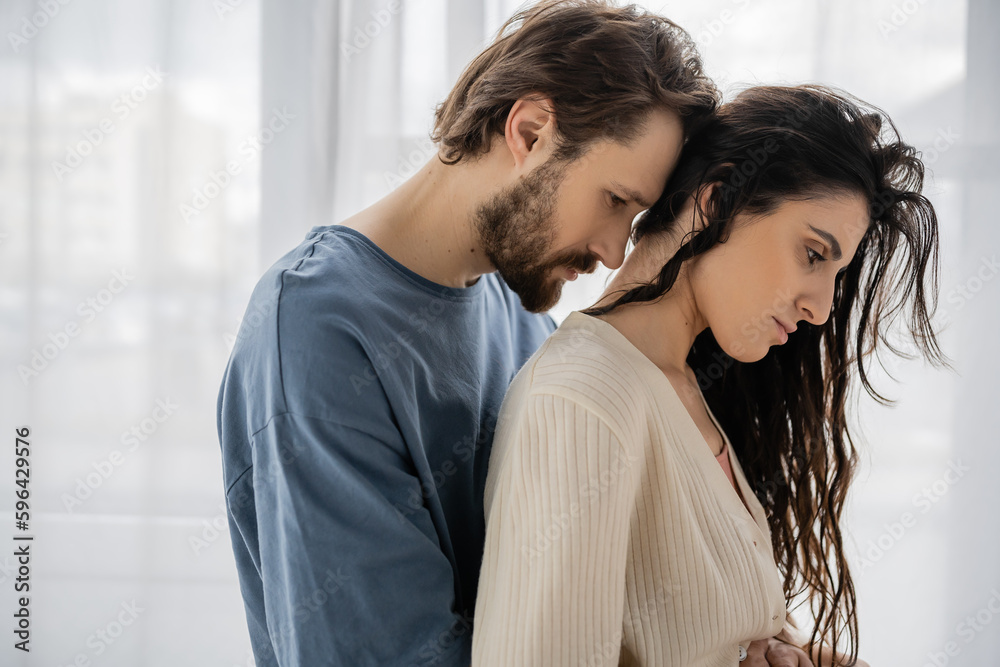 Side view of sad bearded man hugging girlfriend at home. Side view of sad bearded man hugging girlfriend at home.