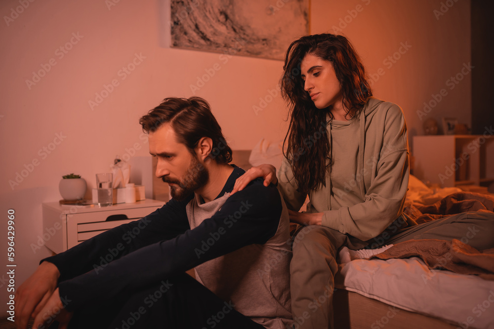 Upset man receiving care from caring girlfriend in bedroom in evening. Upset man receiving care from caring girlfriend in bedroom in evening.