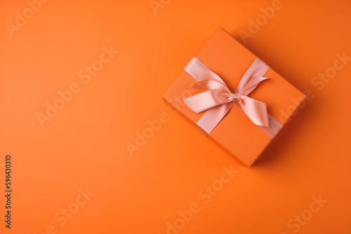 Gift box with satin ribbon and bow on orange background. Holiday gift with copy space. Birthday or Christmas present, flat lay, top view. Christmas giftbox concept