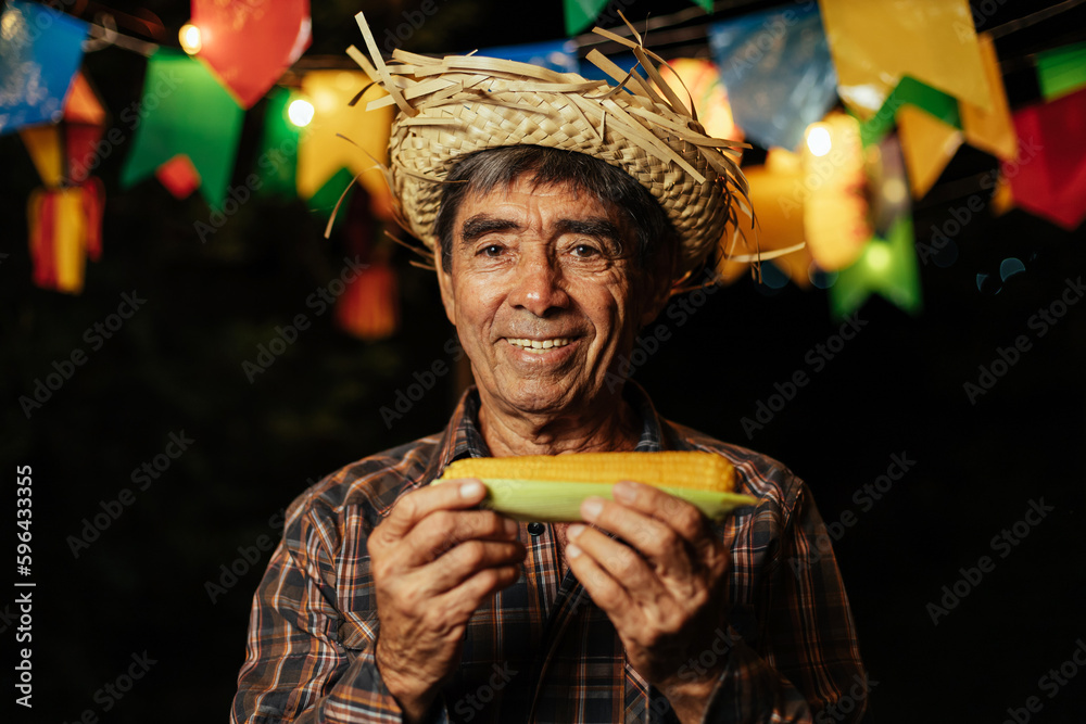 Senior man celebrating the Brazilian Festa Junina. Portrait of a man wearing traditional clothing for the Festa Junina - June festival - eating corn on the cob