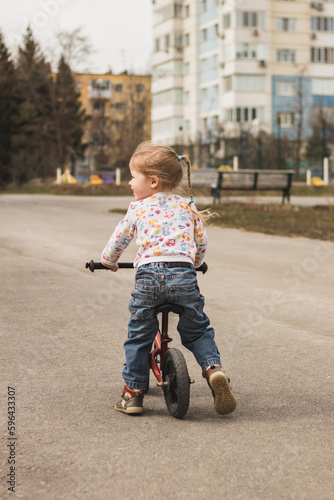 little child girl from behind riding a bike in the city park outdoors