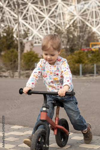cheerful little child girl riding a running bike in the city park in sunny day outdoors