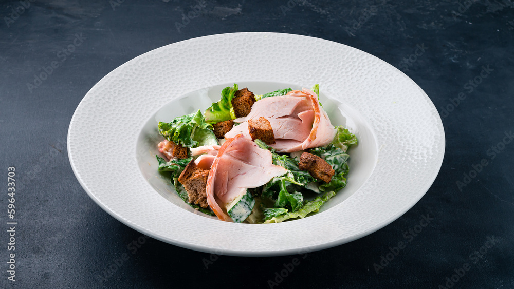 Fresh salad with chicken ham, cucumber, lettuce, croutons and mayonnaise on a dark table.