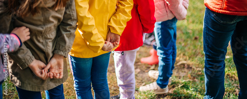 A group of children in colorful clothes are playing a game outdoors, holding their hands behind their backs. The concept of a happy childhood, school.