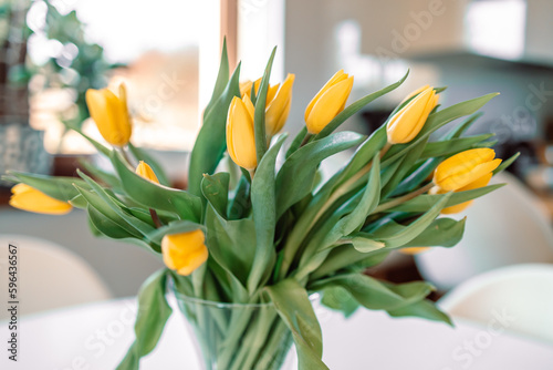 Fototapeta Naklejka Na Ścianę i Meble -  Spring flowers in glass vase on white wooden table in living room. Bouquet of yellow tulips. Contemporary elegant scandi interior. High quality photo