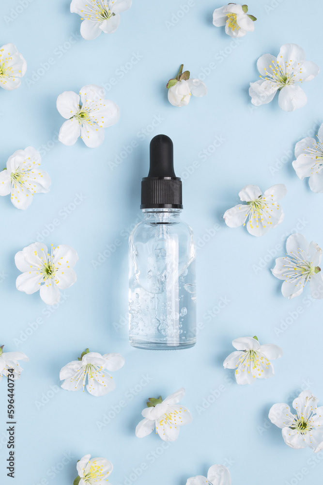 Glass bottle with oil, serum on a blue background with blooming cherry. Herbal homeopathic products. Natural organic spa cosmetics. Glass bottle with oil, serum on a blue background with blooming cherry. Herbal homeopathic products. Natural organic spa cosmetics.